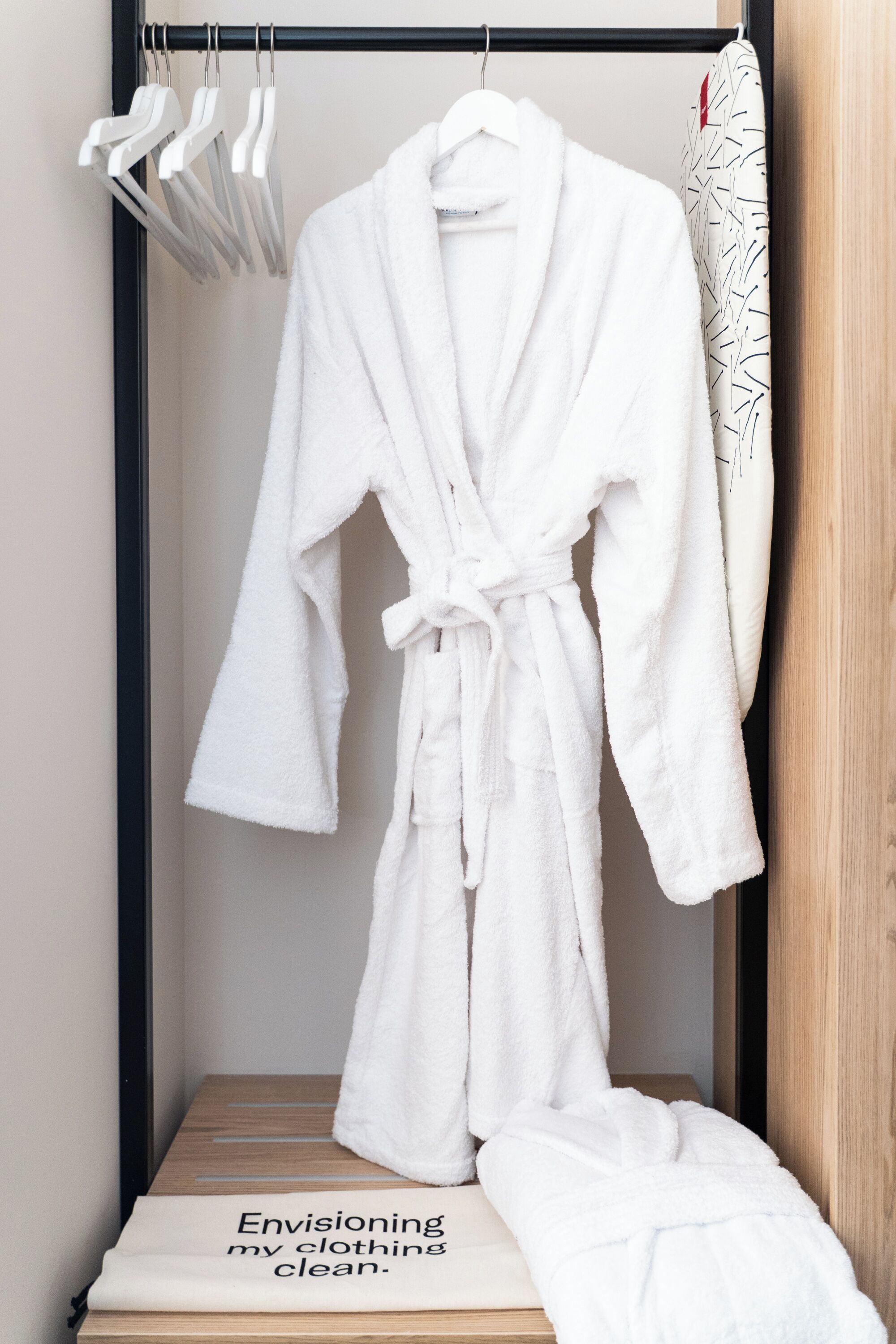 A white bathrobe hanging on a rack with a wooden floor and a sign that reads 'Envisioning my clothing clean.'
