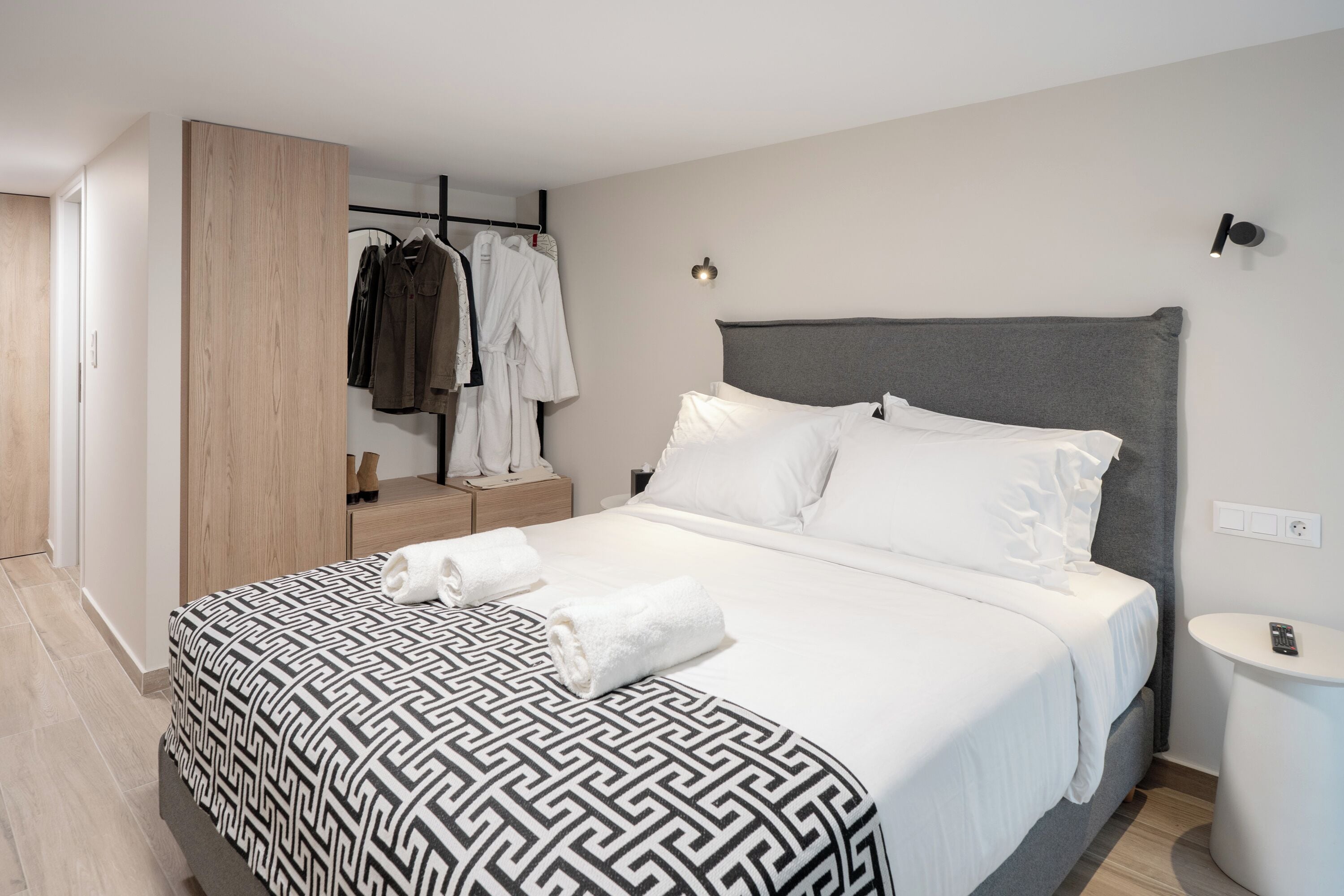 A modern hotel room with a large bed, a wardrobe, a bedside table, and a small round table.