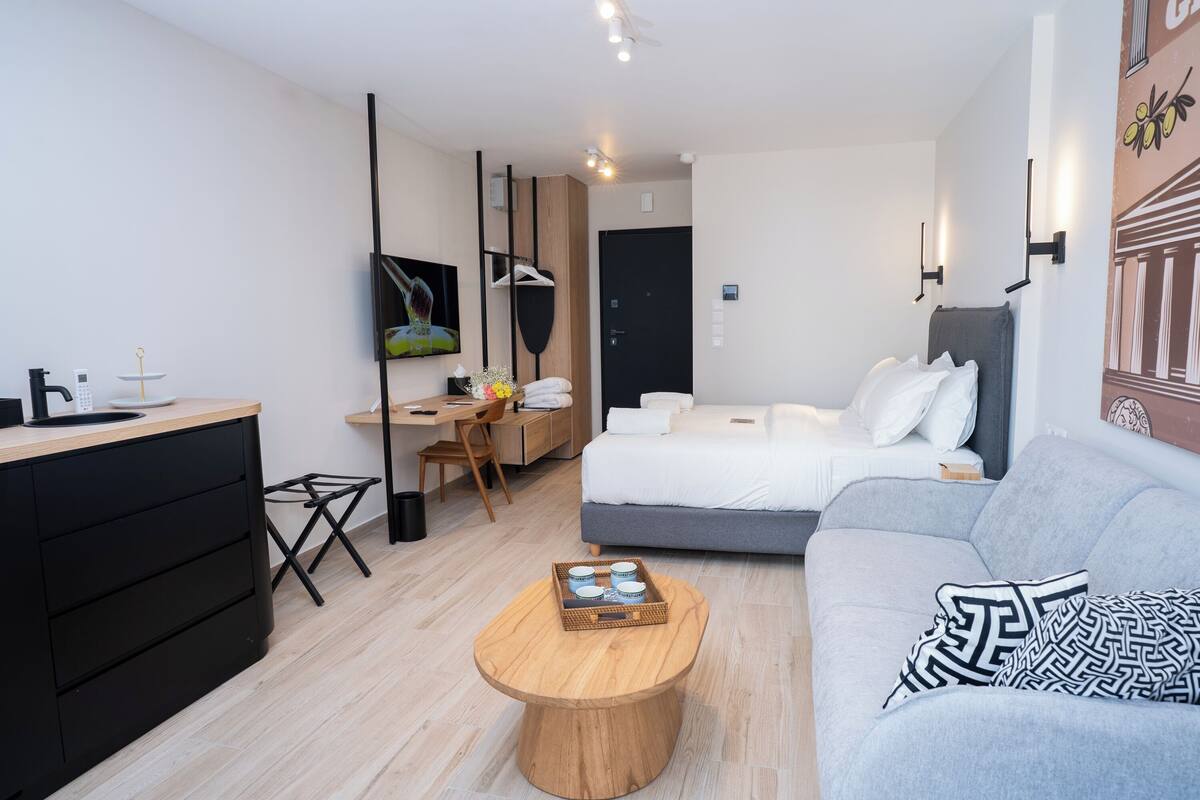 A modern hotel room with a bed, a sofa, a wooden coffee table, a desk, and a TV.