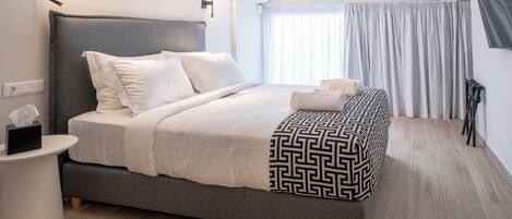 A modern hotel room with a large bed, a bedside table, a wall-mounted air conditioner, and a window with curtains.