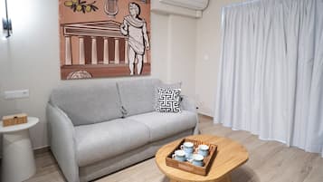 A modern living room with a grey sofa, a coffee table with cups, a wall-mounted air conditioner, and a large decorative poster.