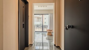 A hallway with a dark door, a glass door leading to an outdoor seating area, and a polished floor. - Vision Lavraga (Athens)