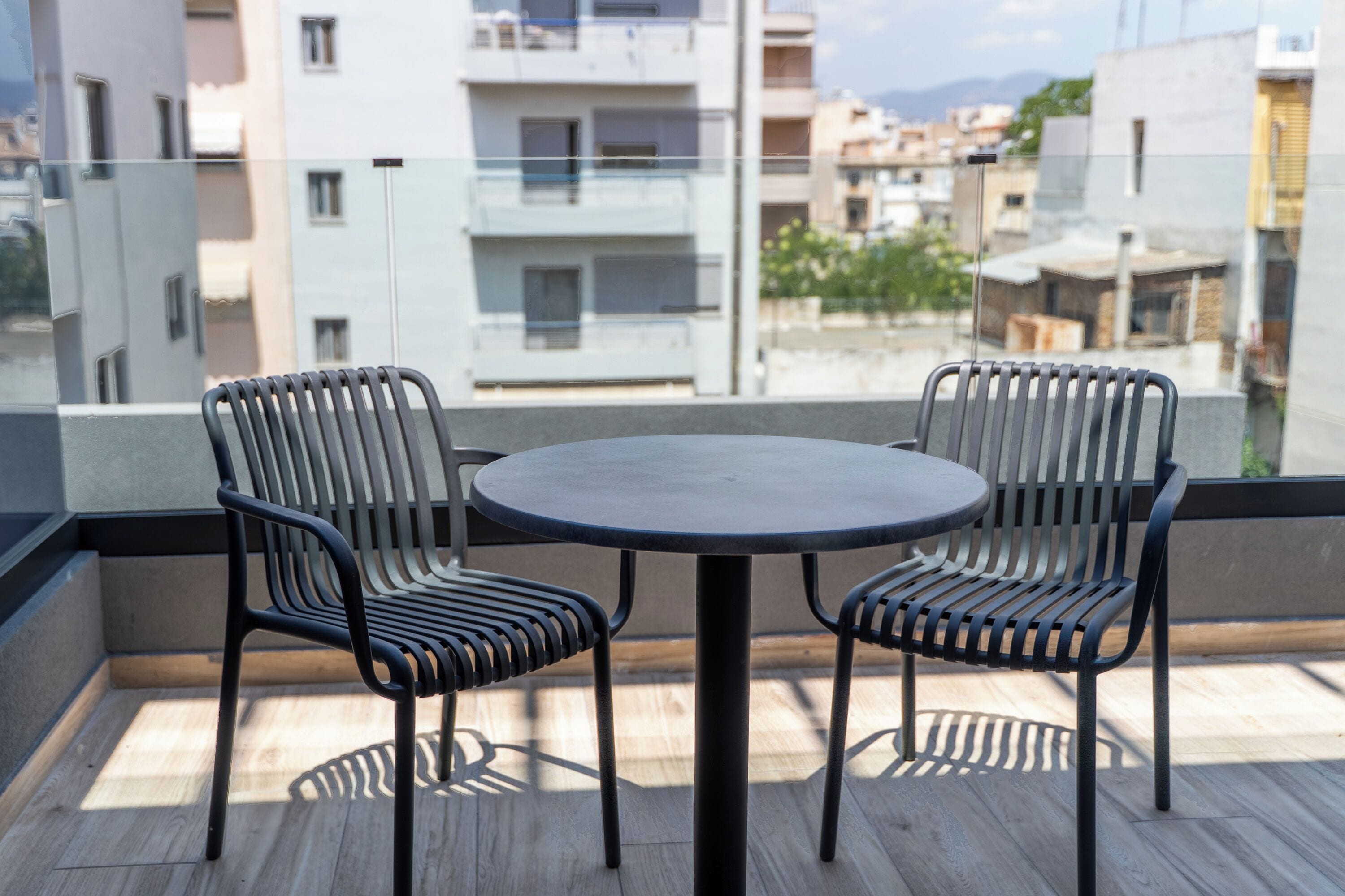 Un balcón con una mesa redonda y dos sillas, con vista a un paisaje urbano que incluye edificios y una montaña al fondo.