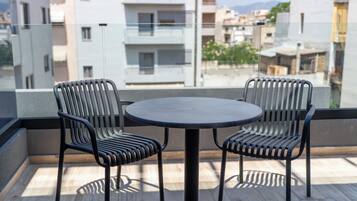 Un balcón con una mesa redonda y dos sillas, con vista a un paisaje urbano que incluye edificios y una montaña al fondo.