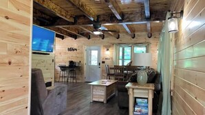 A cozy cabin interior with a wooden ceiling, a television, a sofa, a dining table, and a lamp. - Creekside Cabin with Lake Access , Brand new build !!! (Remsen)