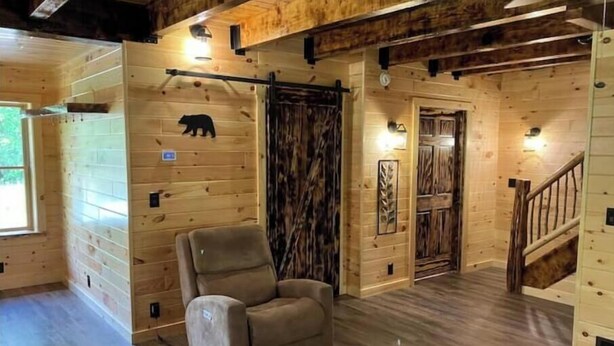 A log cabin interior with a wooden floor, a sofa, a staircase, and a bear decoration on the wall. - Creekside Cabin with Lake Access , Brand new build !!! (Remsen)
