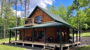 A wooden cabin with a balcony, a covered porch, and a stone foundation. - Creekside Cabin with Lake Access , Brand new build !!! (Remsen)