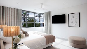 A modern bedroom with a large bed, a flat-screen TV, and a window with a view of palm trees.