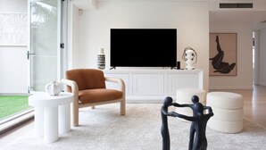 A modern living room with a large flat-screen TV, a brown leather chair, a white console table, and a unique black sculpture.
