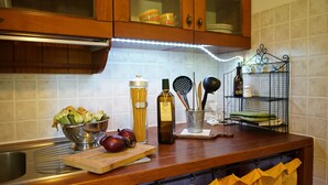 Una cocina con armarios de madera, un lavamanos de acero inoxidable, un colador, una botella de aceite de oliva y una tabla de cortar con verduras.