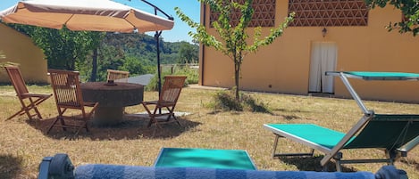Un'area salotto all'aperto con un tavolo rotondo e sedie, un ombrellone e un piccolo albero.