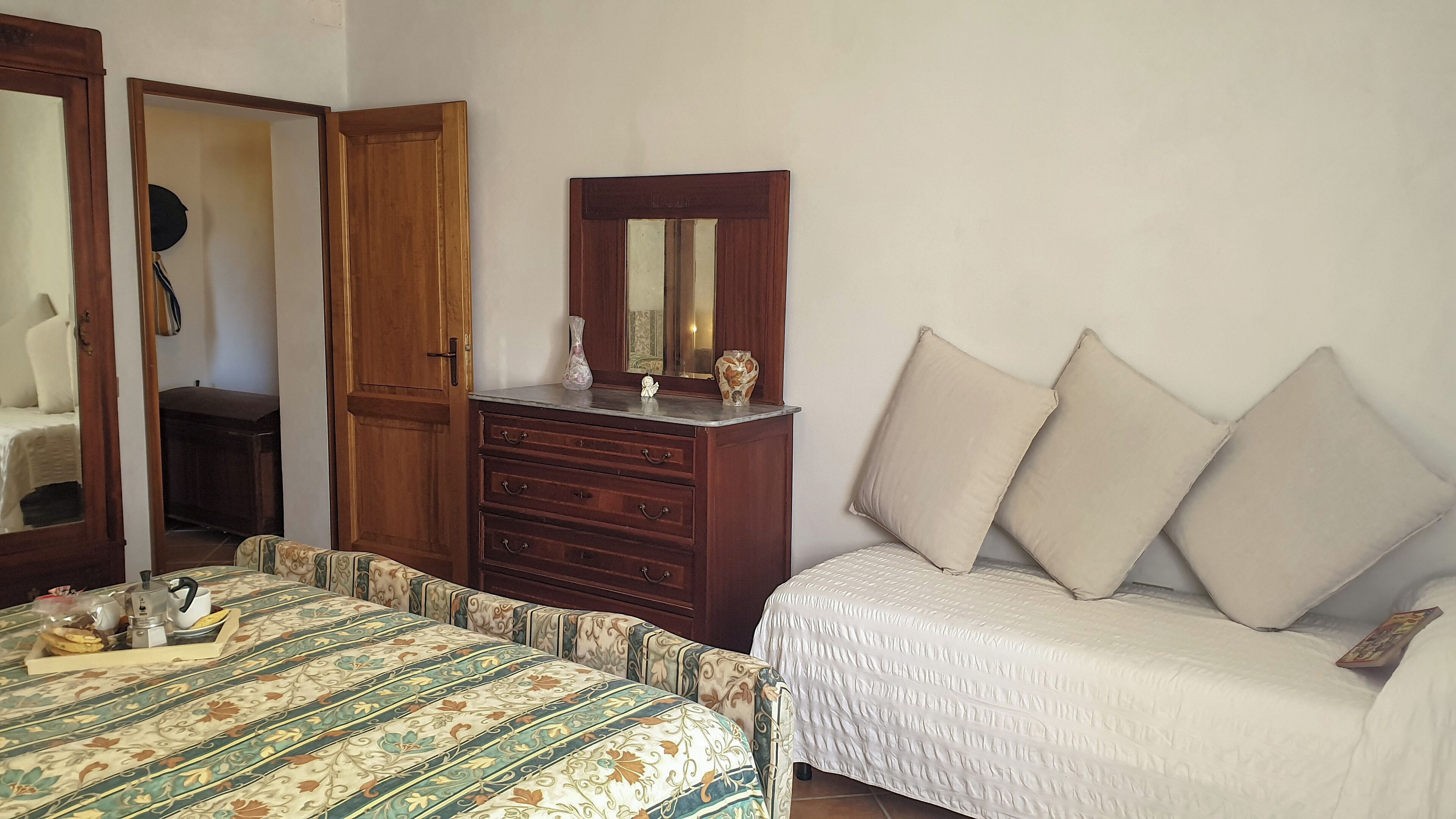 Quarto com cama, cômoda, espelho e mesa de cabeceira com abajur e um vaso.