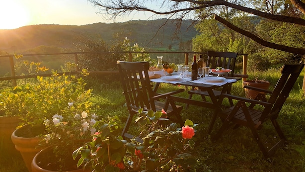 Un área de comedor al aire libre con una mesa preparada para dos personas, rodeada de sillas, y vista a un paisaje montañoso al fondo.