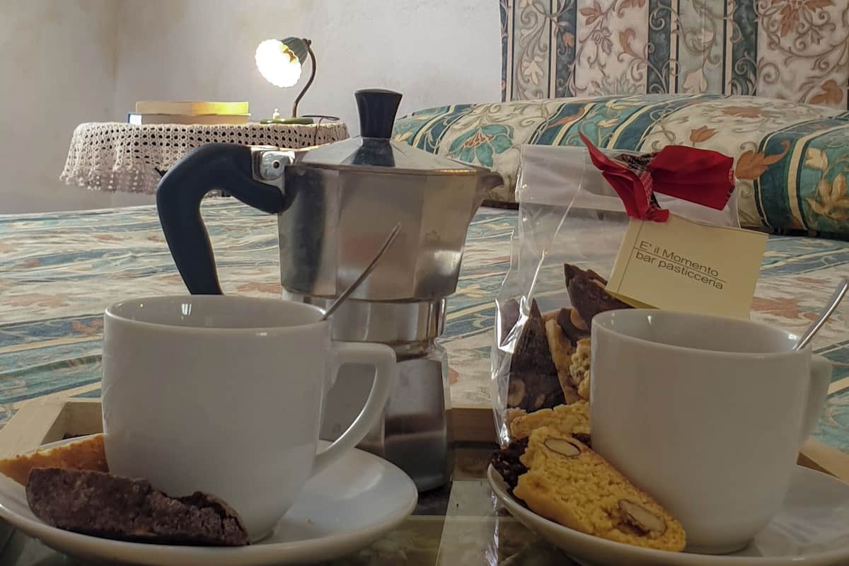 Un plateau de petit-déjeuner avec des viennoiseries et des tasses de café, un mur décoratif orné d’objets suspendus et un couvre-lit à motifs.