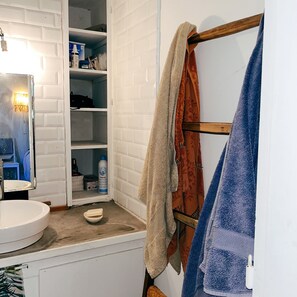 Et badeværelse med en hvid vask, et spejl, en håndklædestang med tre håndklæder og en hylde med toiletartikler.