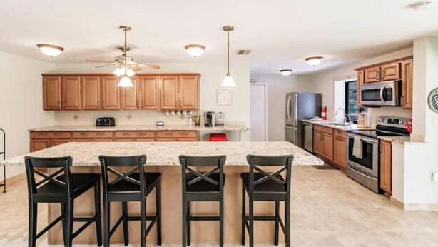 A modern kitchen with wooden cabinets, a large island with bar stools, stainless steel appliances, and pendant lighting. - Boater's Paradise-Lux 3 br w/ private heated pool,bring your 27 ft boat! (Port Charlotte)