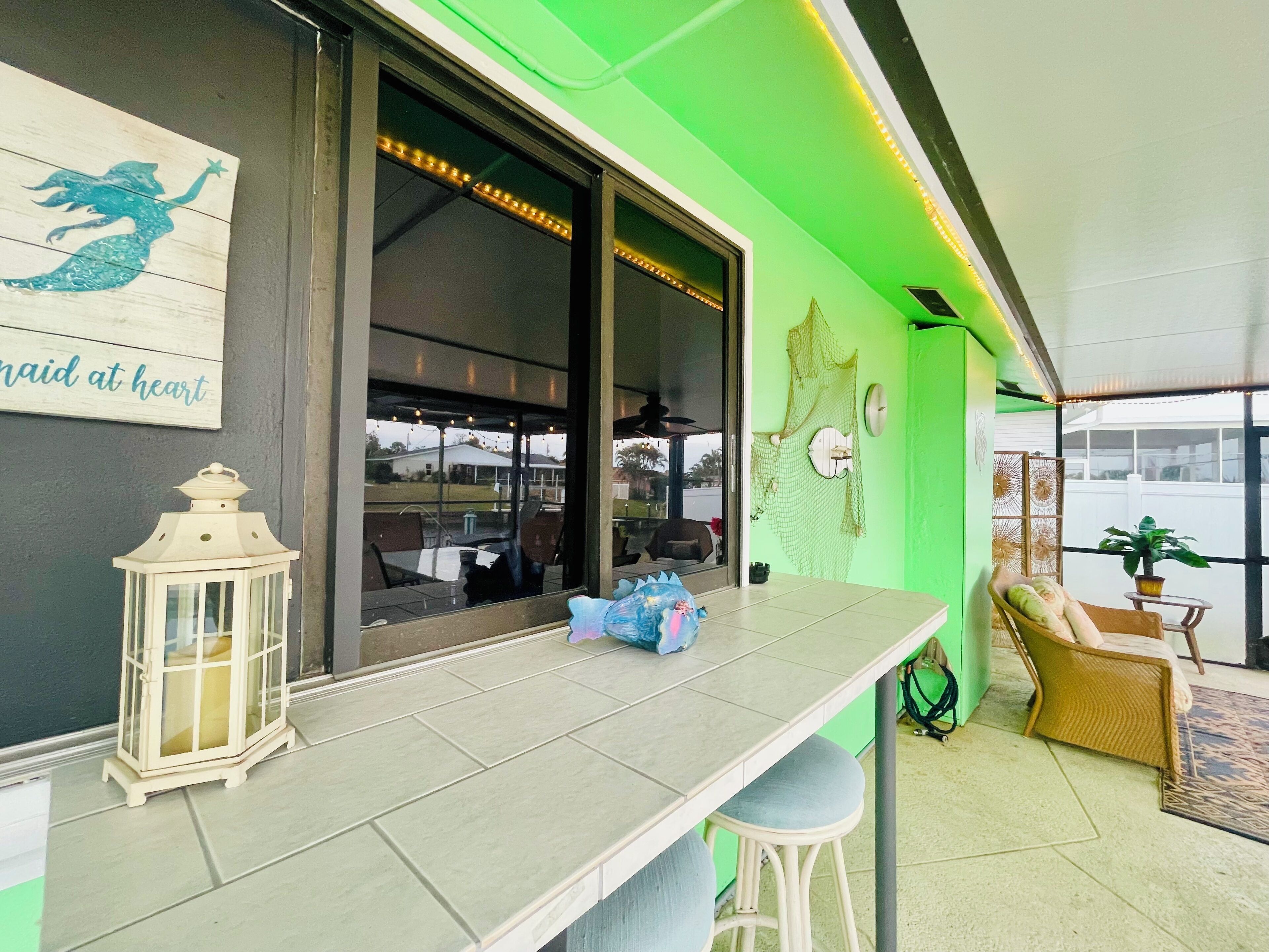 A room with a green accent wall, a white table with a lantern, a chair, and a view of the outside.