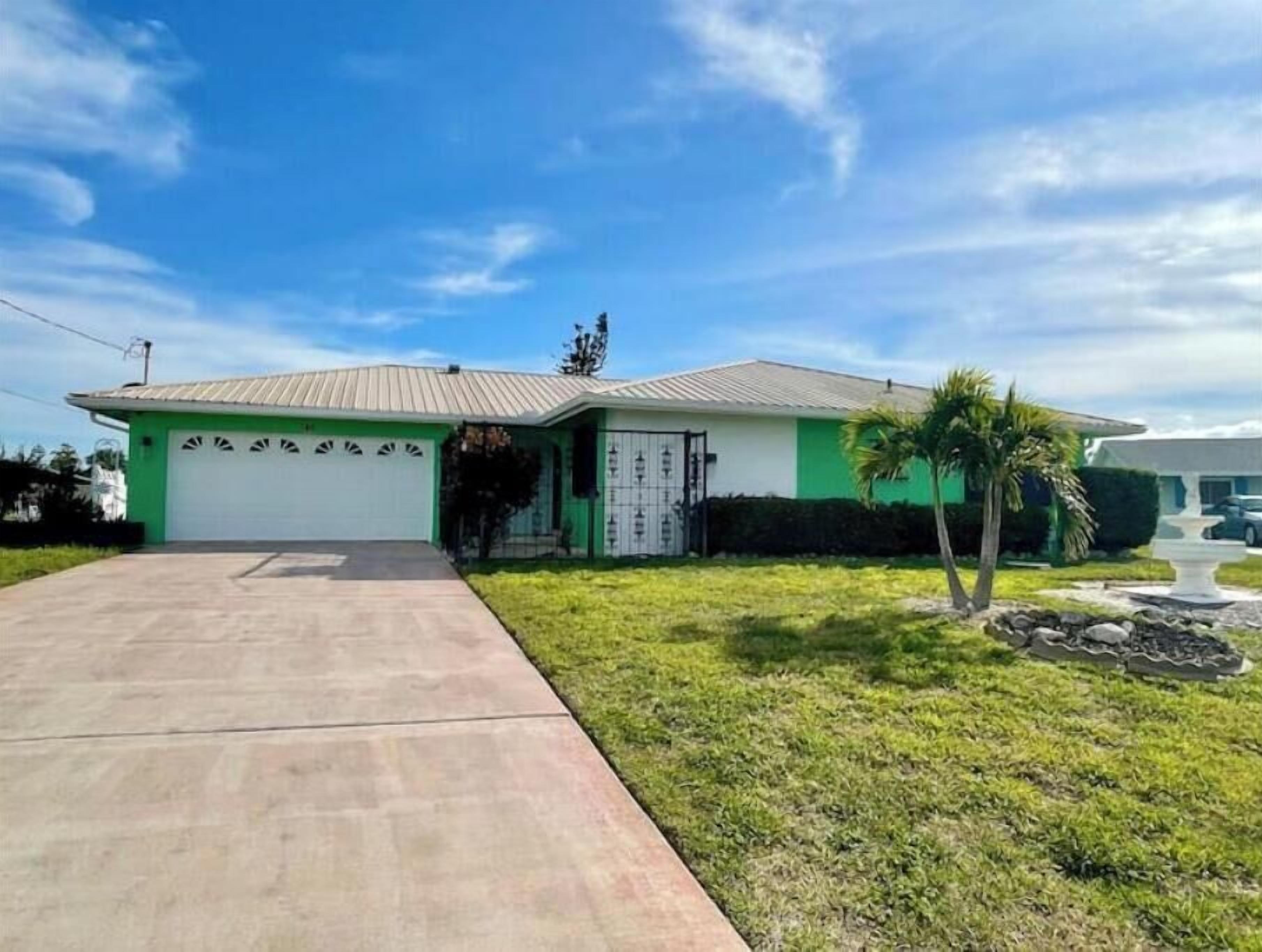 Una casa de una sola planta con garaje, un pequeño jardín delantero y una palmera.