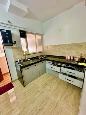 Een koelkast, een kookplaat, kookgerei, borden en bestek, eettafels