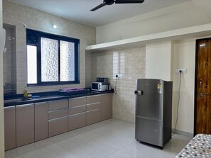 A kitchen with a refrigerator, microwave, and a window with patterned blinds.