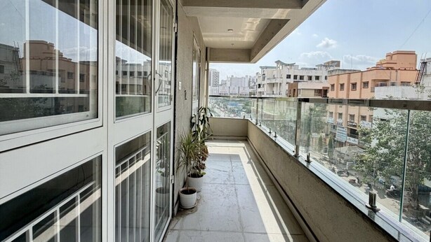 A balcony with large windows, potted plants, and a view of surrounding buildings. - Owl's Retreat: 2BHK Modern AC Flat in Wakad, Pune (Pimpri-Chinchwad)