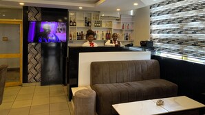 A bar area with a TV screen, seating, and shelves with bottles.