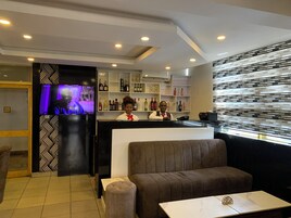 Zona de bar con pantalla de televisión, asientos y estantes con botellas.