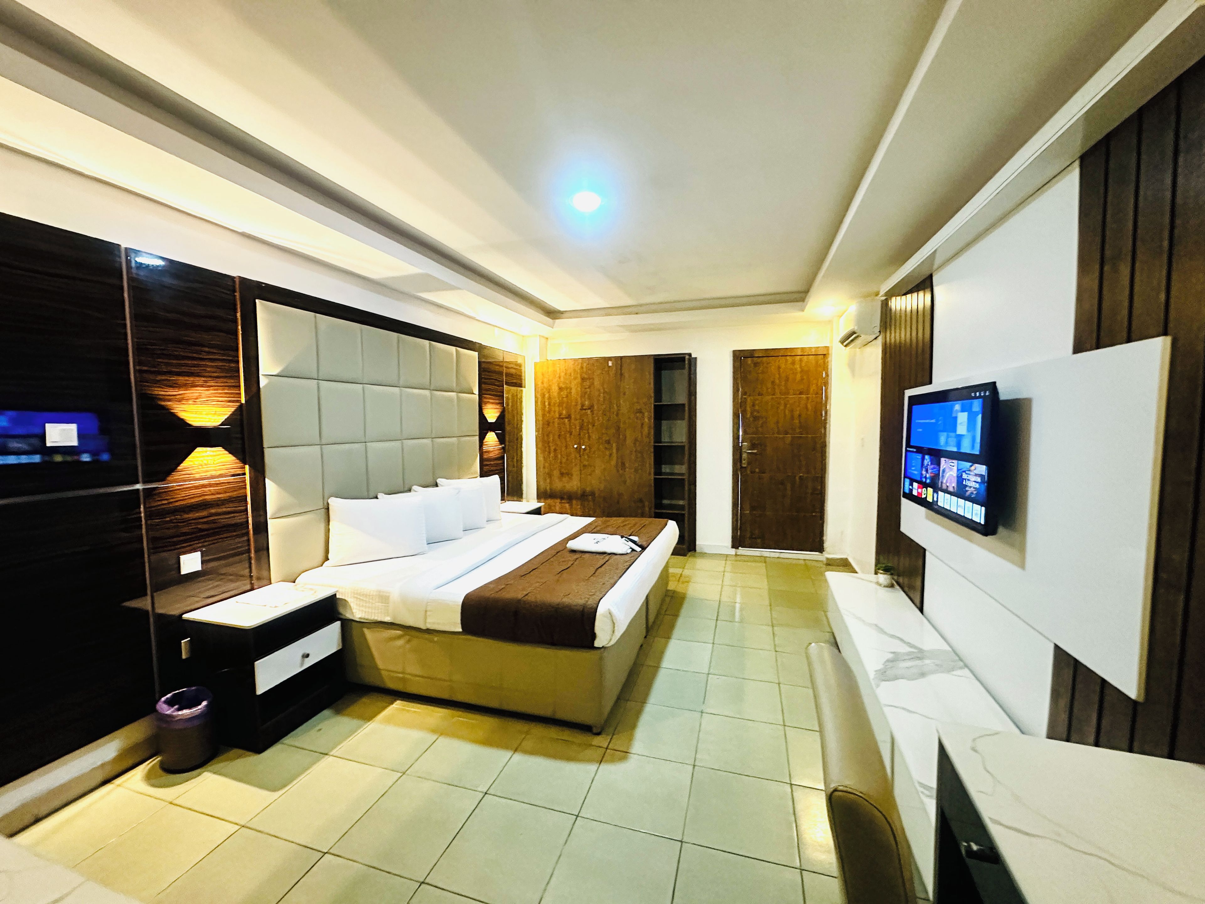A modern hotel room with a large bed, a TV mounted on the wall, and a wooden wardrobe.