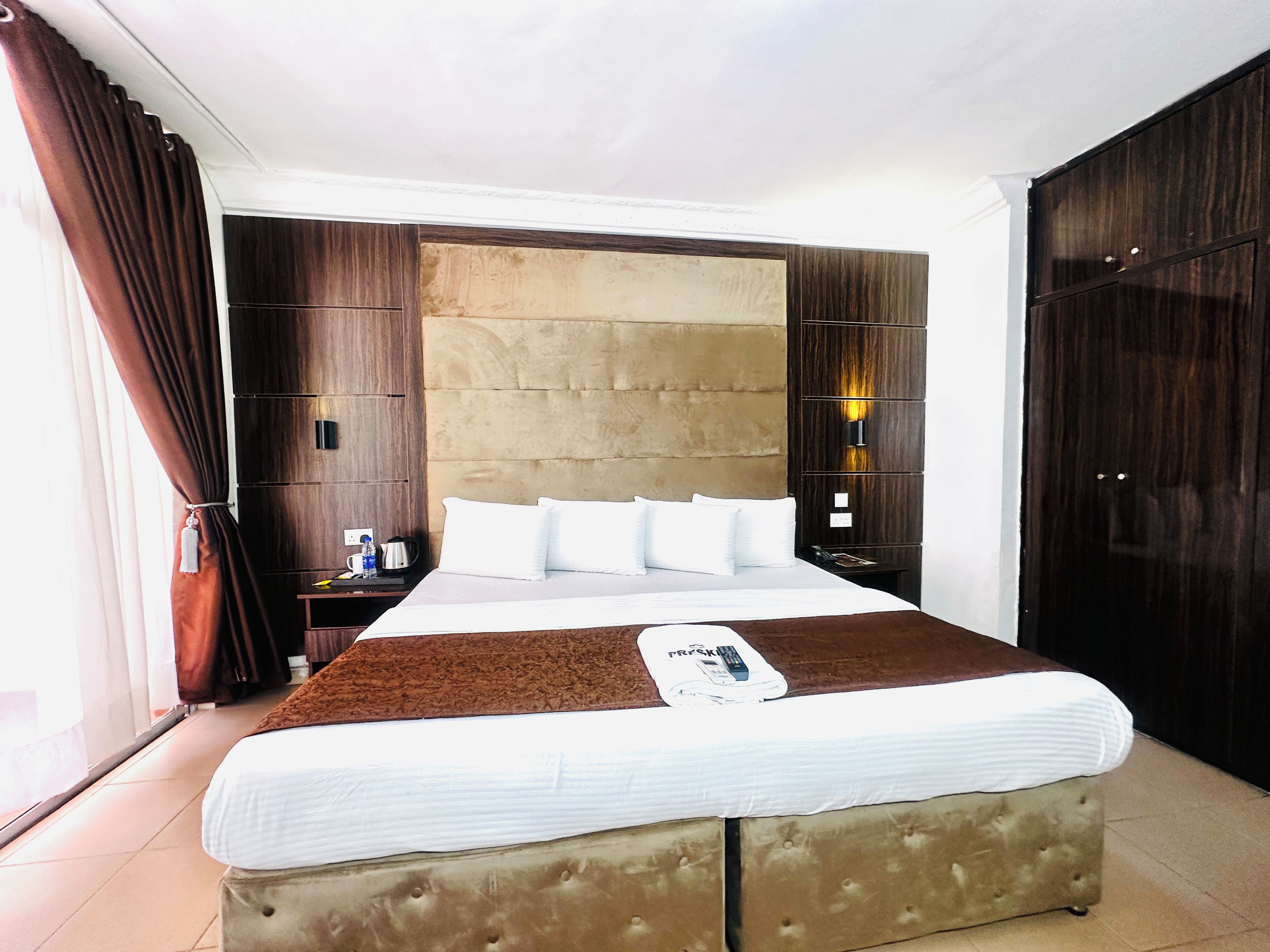 A hotel room with a large bed, a headboard, a nightstand, and a wardrobe.