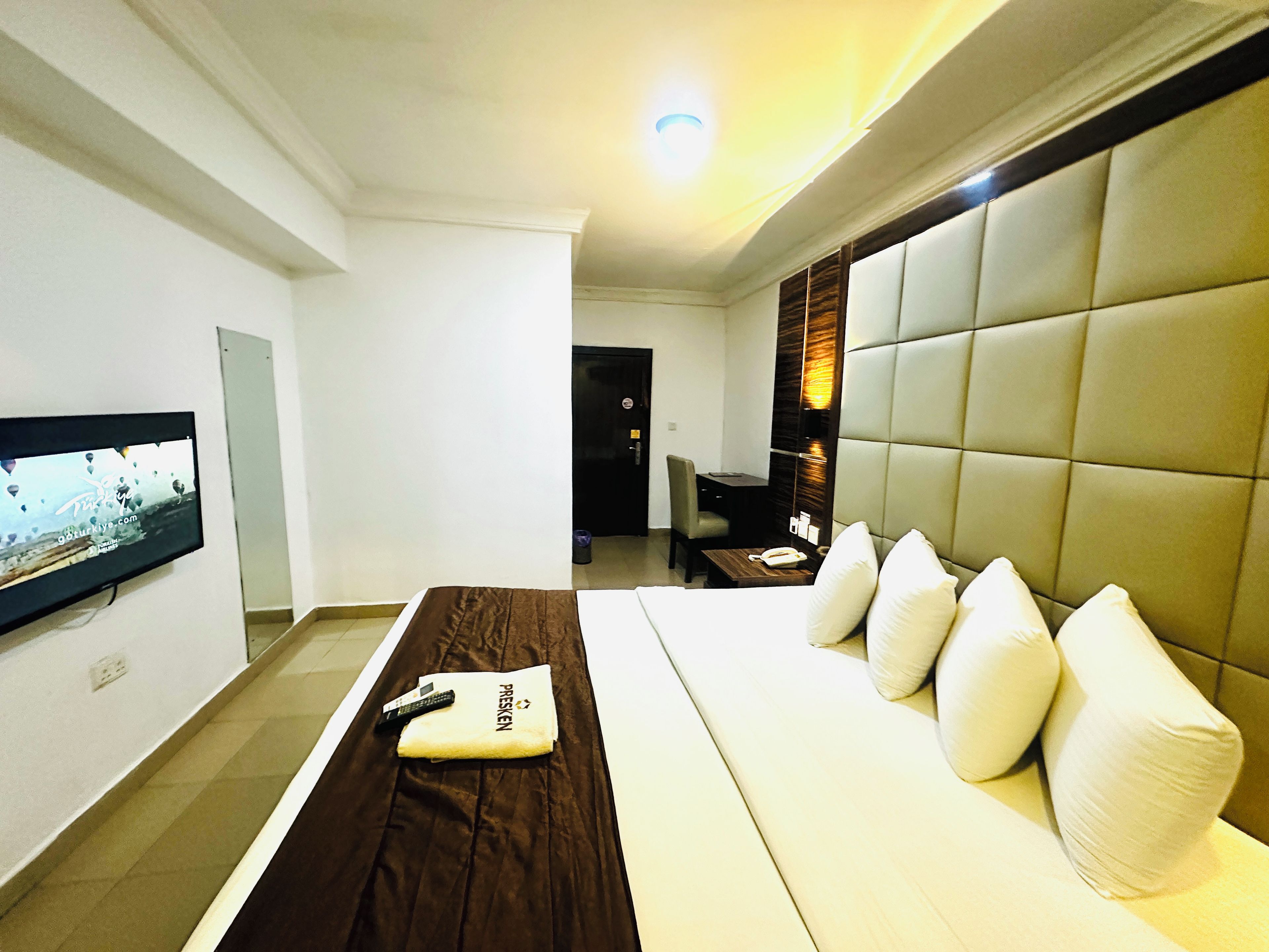 Ein Hotelzimmer mit Bett, Wandfernseher, Schreibtisch mit Stuhl und einer Couch mit Kissen.