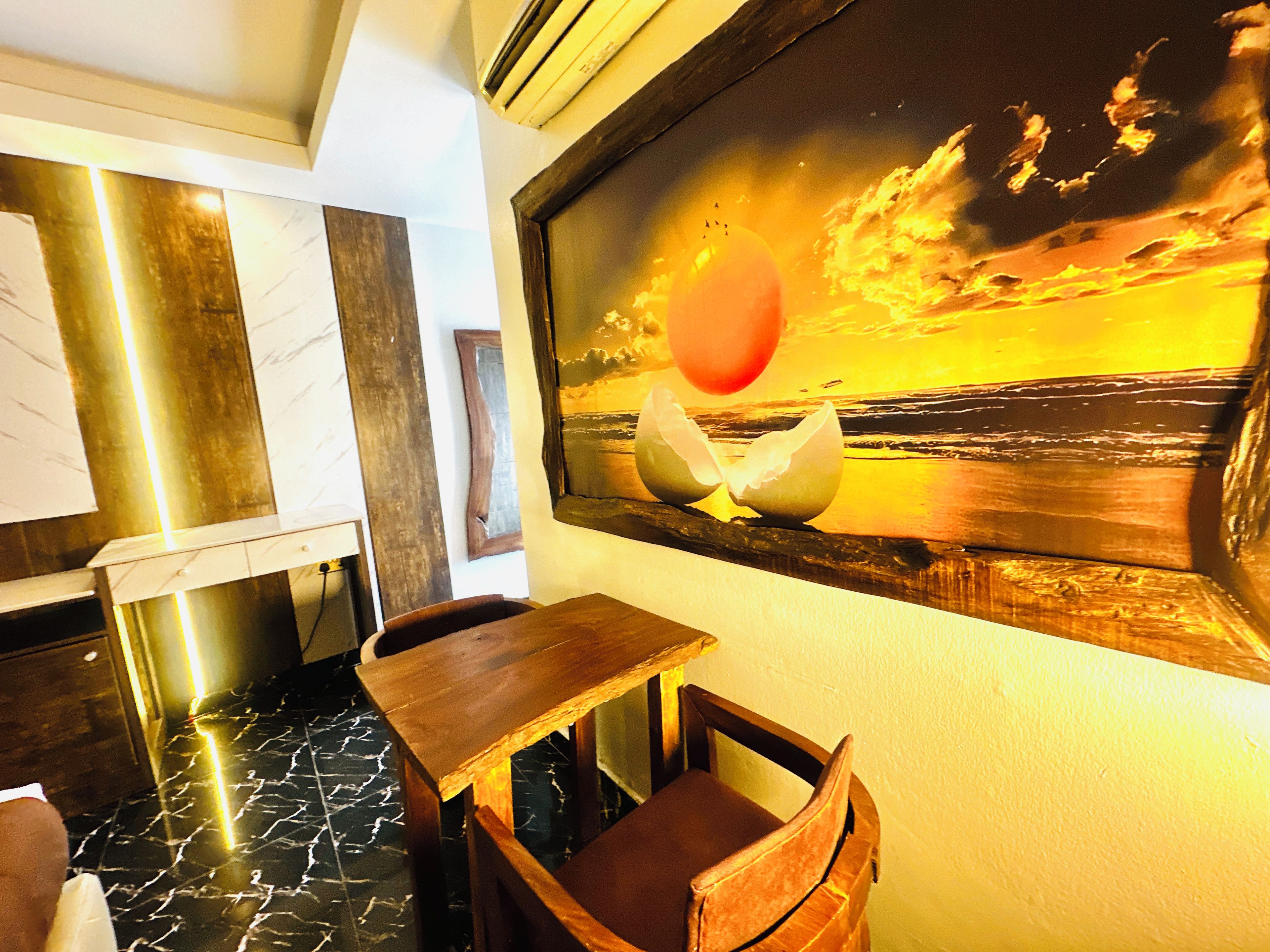 A room with a wooden table, a chair, a marble floor, and a painting of a sunset over the ocean.