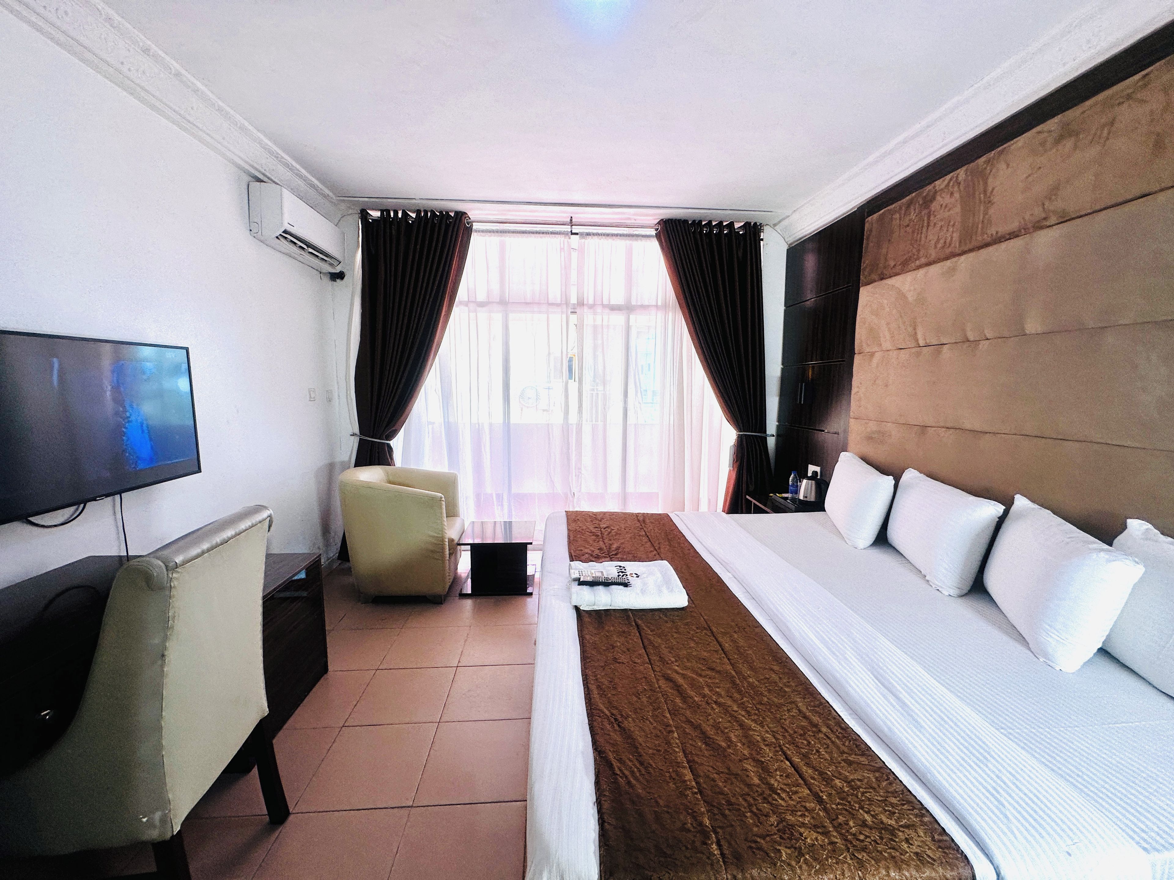 Ein Hotelzimmer mit Bett, Fernseher, Sessel und Vorhängen.