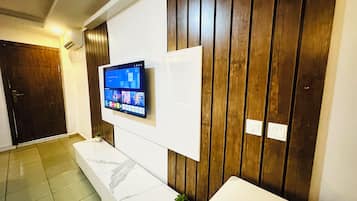 Un lobby moderno de hotel con una televisión de pantalla plana montada en una pared de paneles de madera, un banco de mármol y una puerta.