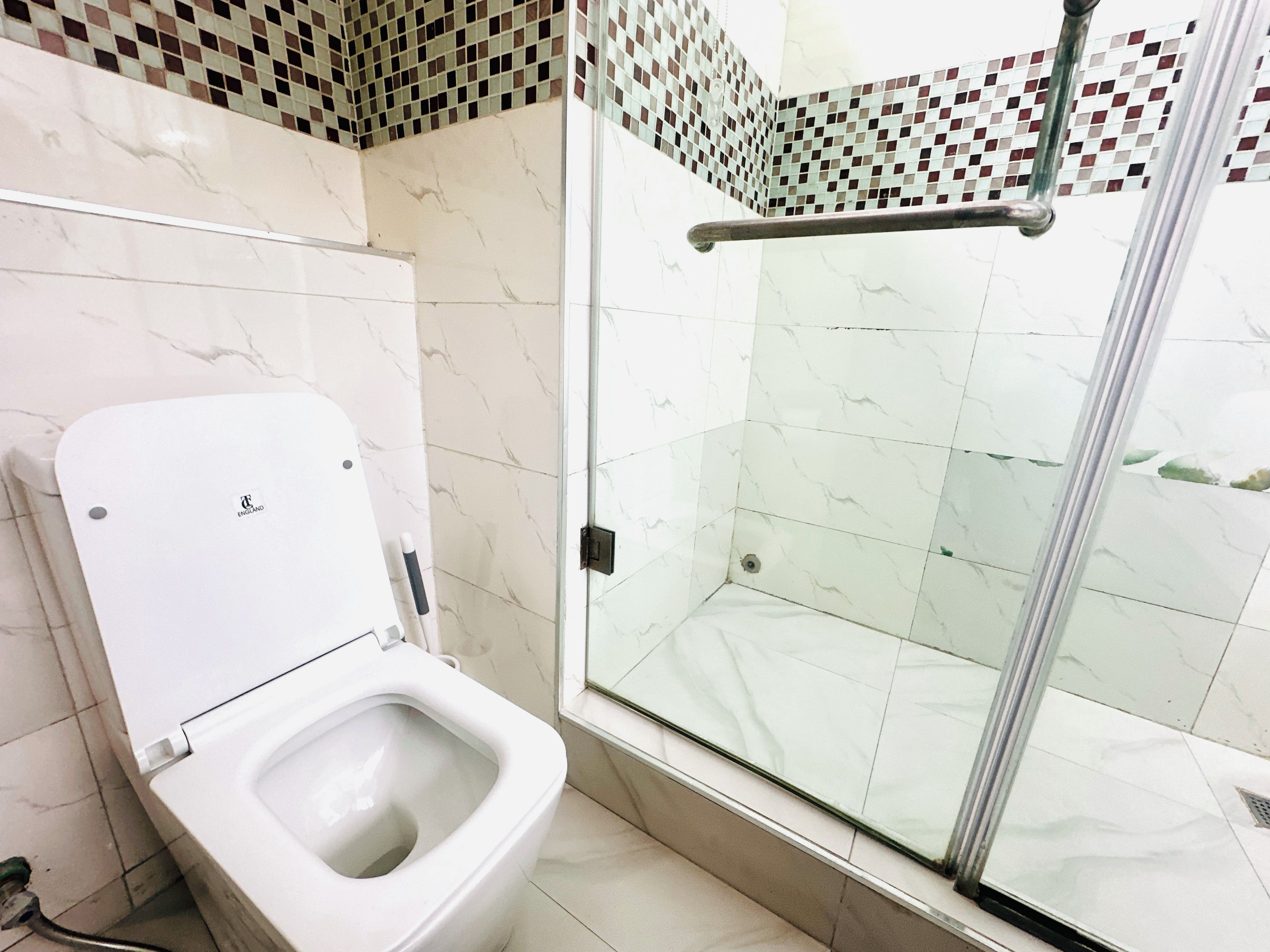 A bathroom with a toilet, a shower with a glass door, and a tiled floor.