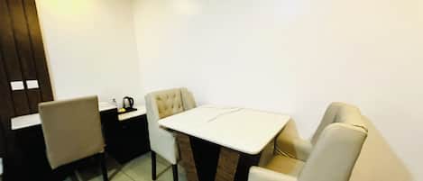 Un comedor con una mesa y cuatro sillas, una mesita con un hervidor y un mueble de color oscuro.