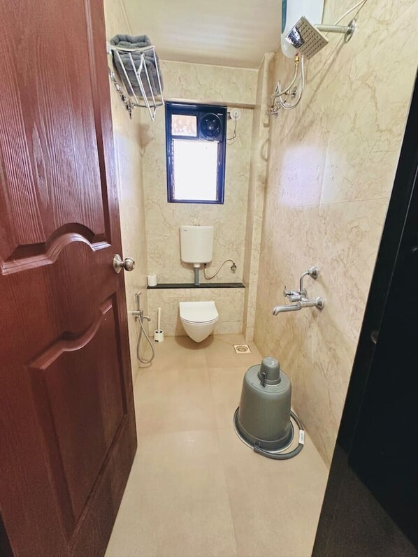 Un baño pequeño y funcional con inodoro, una ventana, ducha y un perchero para toallas.