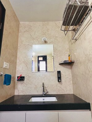 Een badkamer met een wastafel, spiegel, handdoekrek en een klein plankje met toiletartikelen.