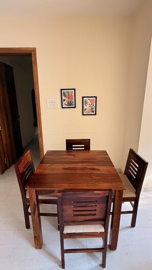 Een eethoek met een houten tafel en vier stoelen, twee ingelijste kunstwerken aan de muur, en een zichtbaar stopcontact.