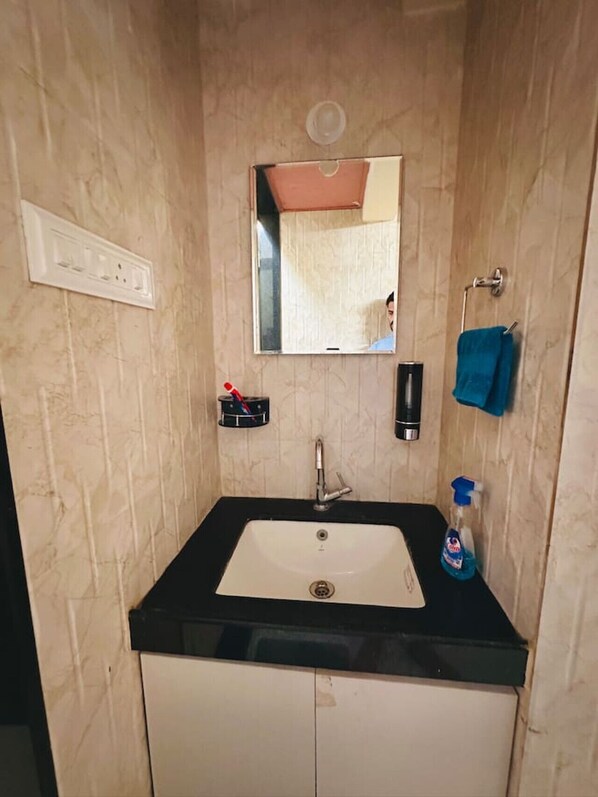 A bathroom with a sink, mirror, towel rack, and a bottle of hand soap.