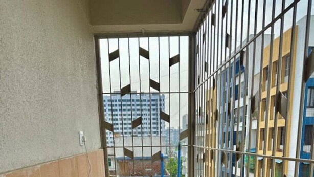 Un corredor estrecho con una reja de metal, una puerta negra y una escalera metálica apoyada en la pared.