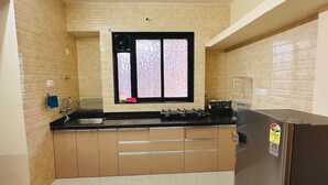 Una cocina con paredes de baldosas color beige, un ventilador de techo negro, un ventanal con vidrio esmerilado y un refrigerador de acero inoxidable.