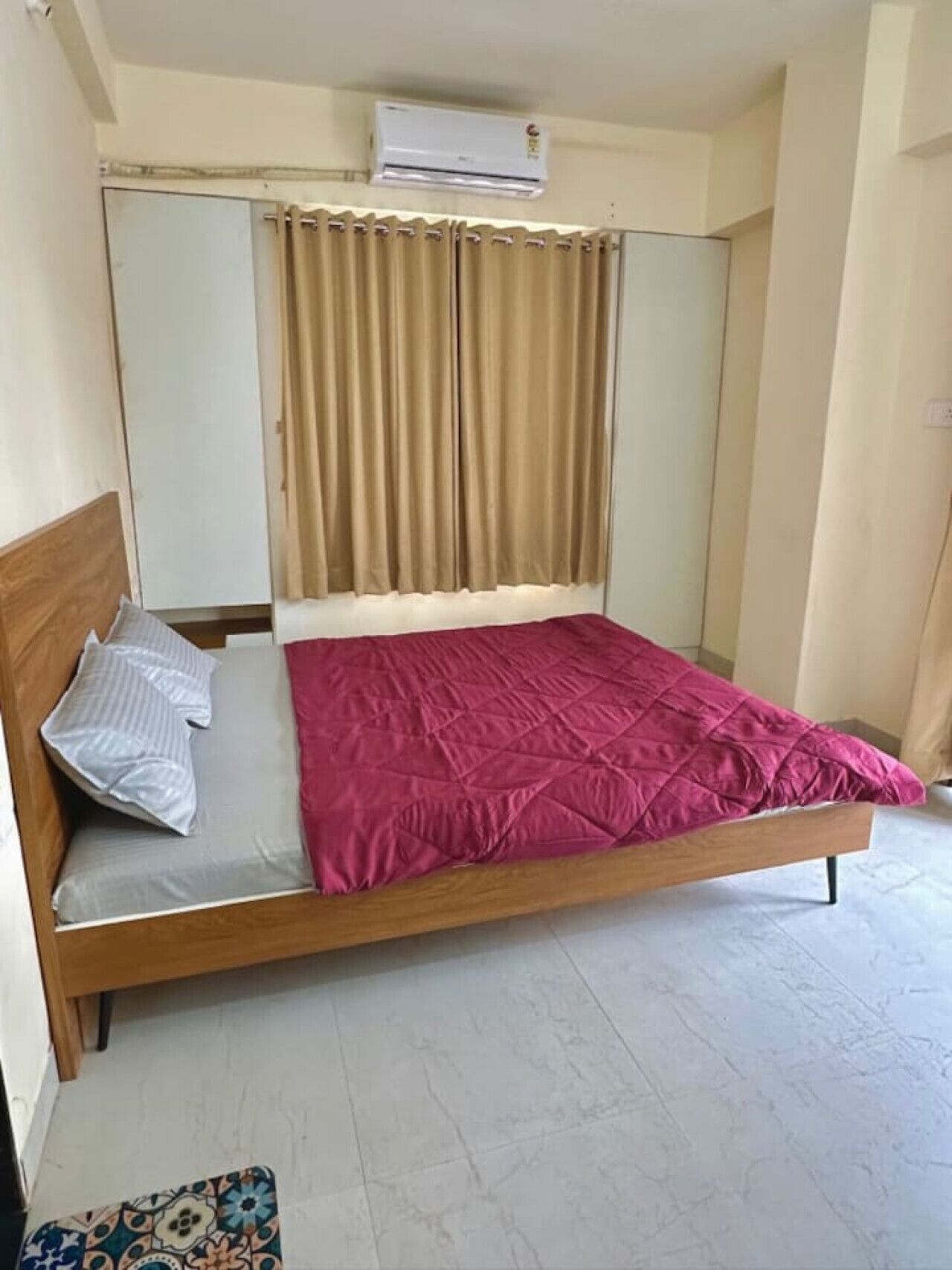 Een enkel bed met houten frame, een roze deken en een grijs kussen.