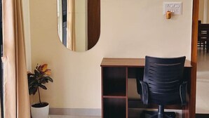 A hotel room with a bed, a desk, a chair, a potted plant, and a mirror on the wall. - Robin`s Roost: 2BHK Modern AC Flat in Wakad, Pune (Pimpri-Chinchwad)