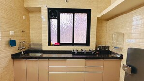 Una cocina con cubierta negra, armarios color crema y un ventanal con vidrio esmerilado, además de un refrigerador de acero inoxidable.