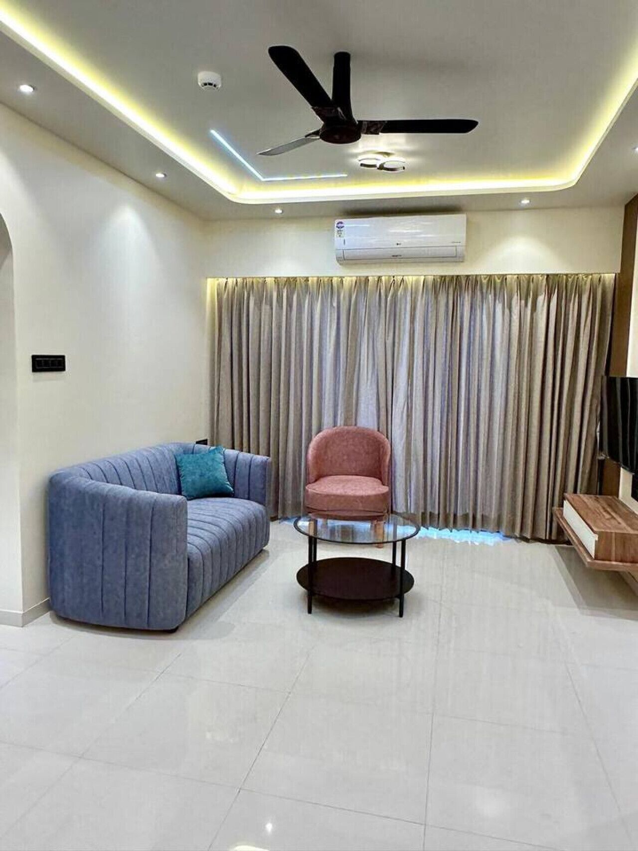 Un salon moderne doté d’un ventilateur de plafond, d’un canapé, d’un fauteuil, d’une table basse en verre et d’un meuble pour la télévision.
