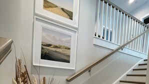 A staircase with wooden steps and a metal handrail, leading to a landing with two framed landscape photographs. - Beach block/Ocean View 82nd Street (Ocean City)