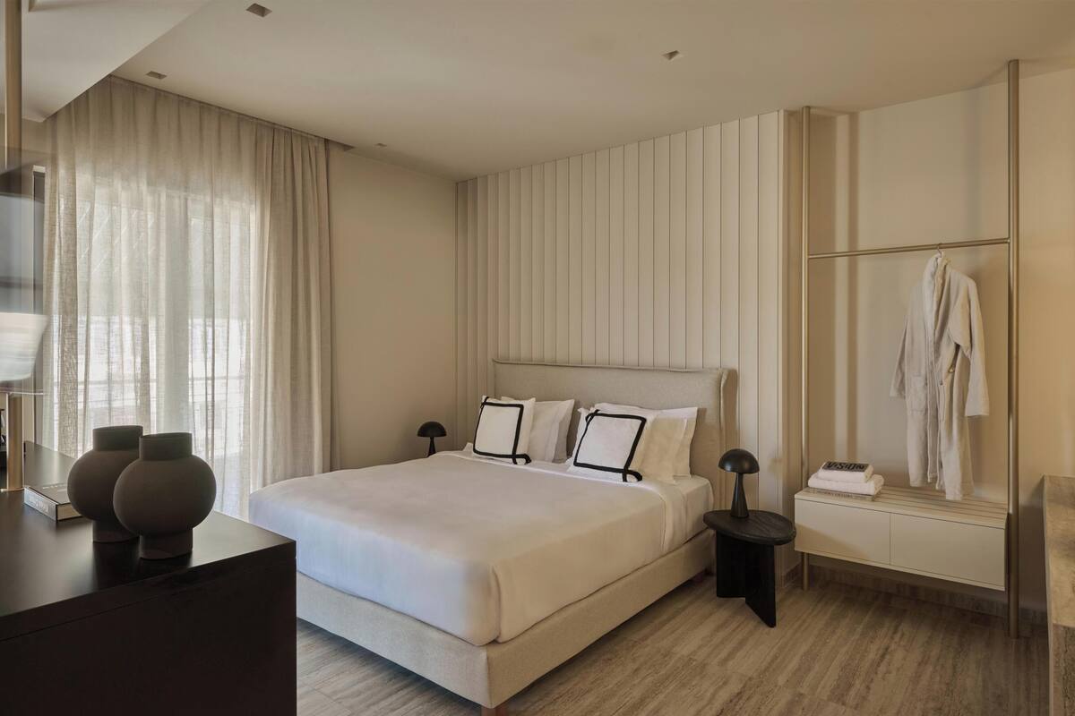 A modern hotel room with a large bed, bedside tables, a wardrobe, and a mirror.