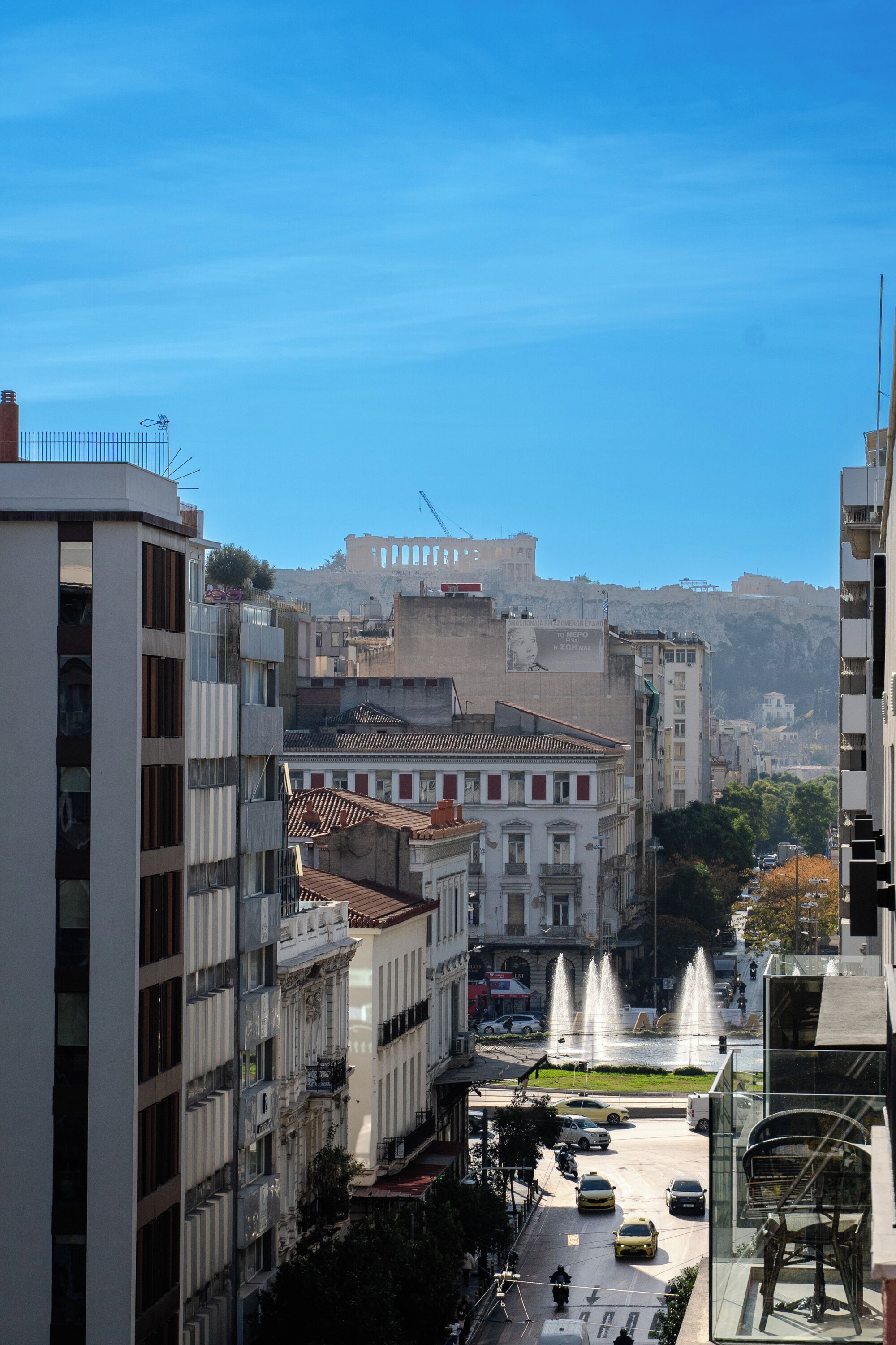 A city street with buildings, a fountain, and a clear sky.