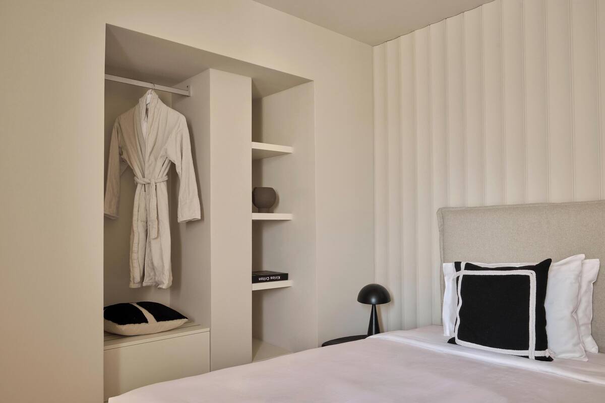 A hotel room with a bed, a bedside table, a lamp, a wardrobe, and a window with blinds.