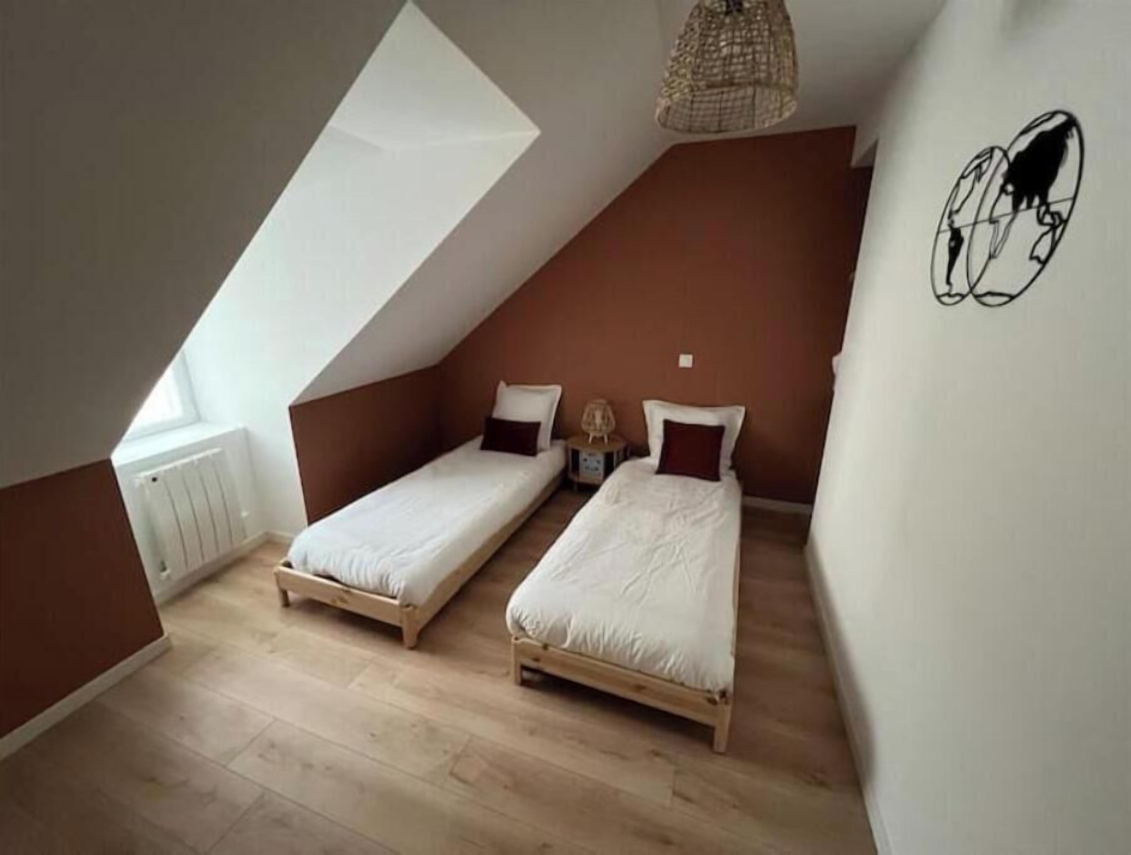 A small, sloped-roofed room with two single beds, a radiator, and a hanging light fixture.